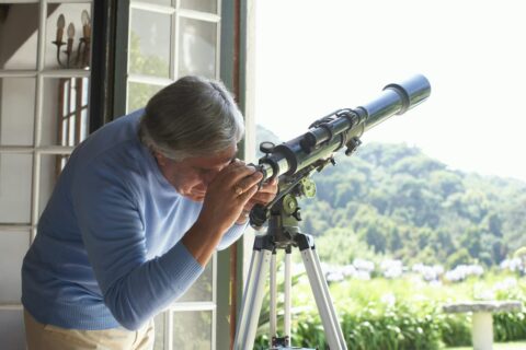 Mann beobachtet durch ein Fernrohr im Garten