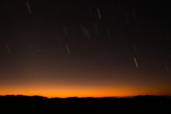 Meteorschauer am Nachthimmel mit Sternschnuppen über einer Bergsilhouette bei Sonnenuntergang